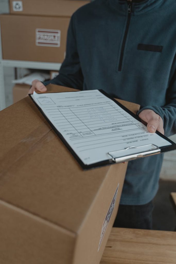 Person in a warehouse holding a box with a shipping checklist on a clipboard.