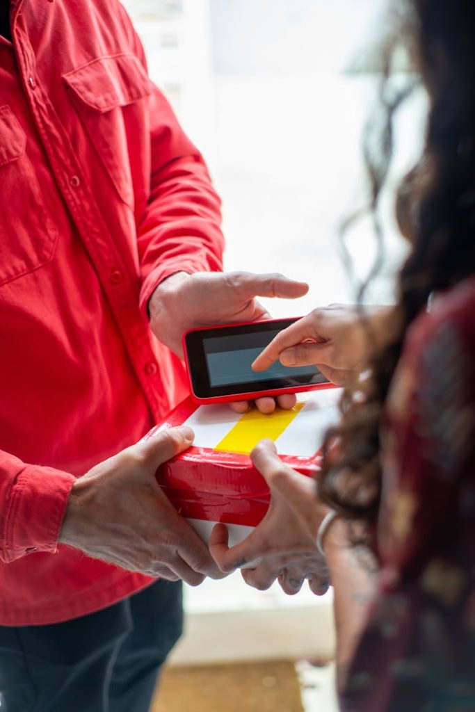 A delivery person in red hands a package to a customer for electronic signature, highlighting e-commerce convenience.